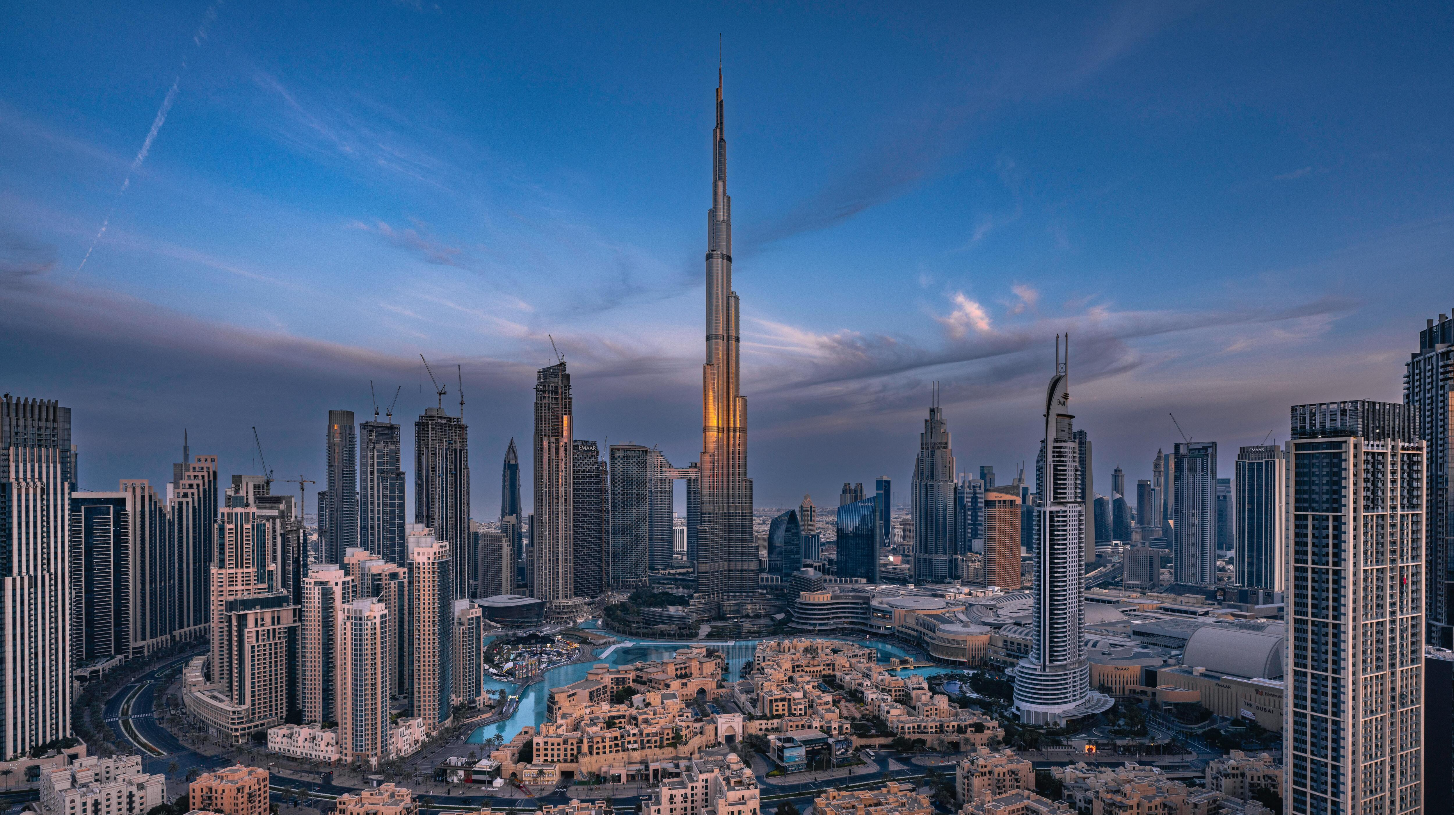 Dubai skyline at night with skyscrapers, including Burj Khalifa, illuminated in AW Connect brand colors of yellow, orange, blue, and navy.